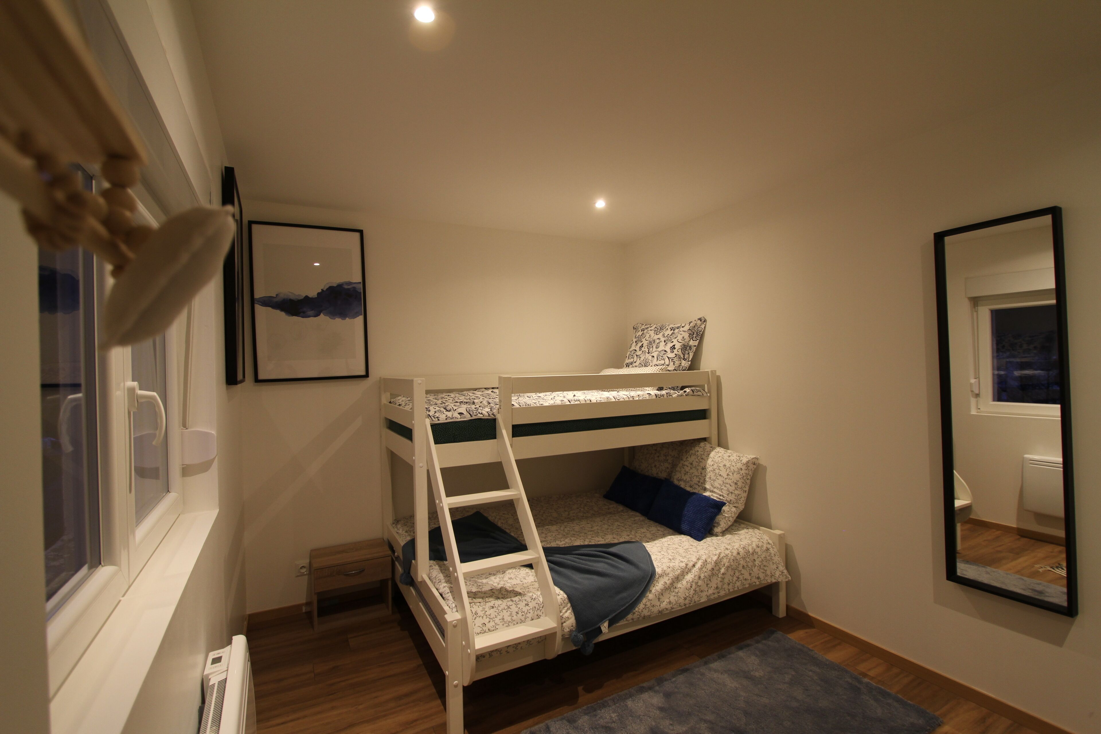 Habitación con literas, una escalera, ventana, radiador y espejo en la pared.