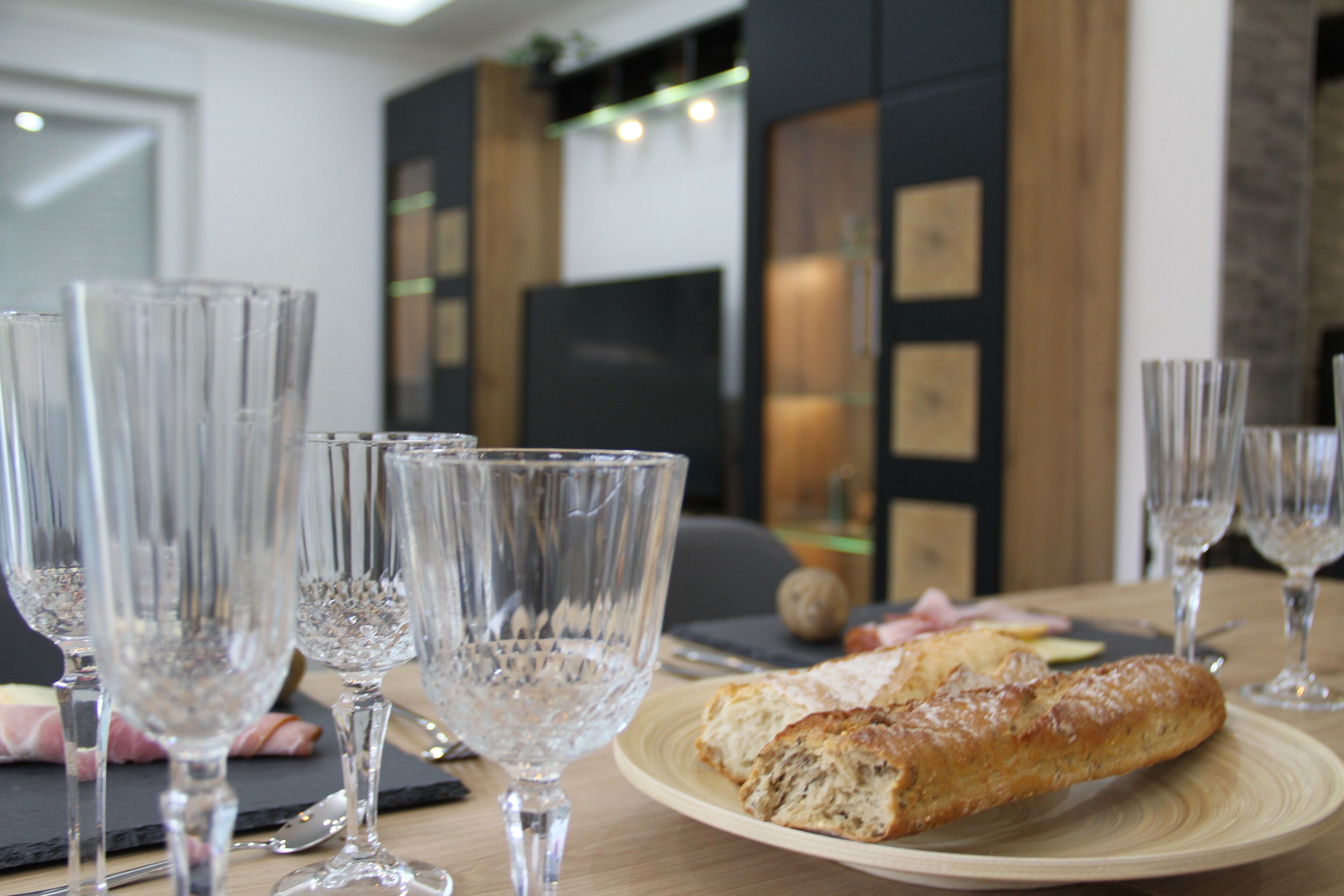 Een eettafel met meerdere glazen heldere wijn en een bord eten, inclusief een baguette en vlees.