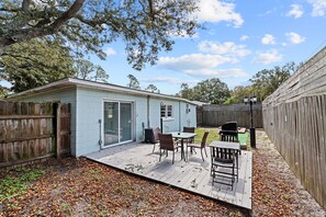 A small, light blue shed with a sliding glass door, a patio with a table and chairs, and a wooden fence surrounding the area. - Coastal Cabana ~ Cozy getaway in the heart of town w/a privately fenced backyard (Panama City Beach)