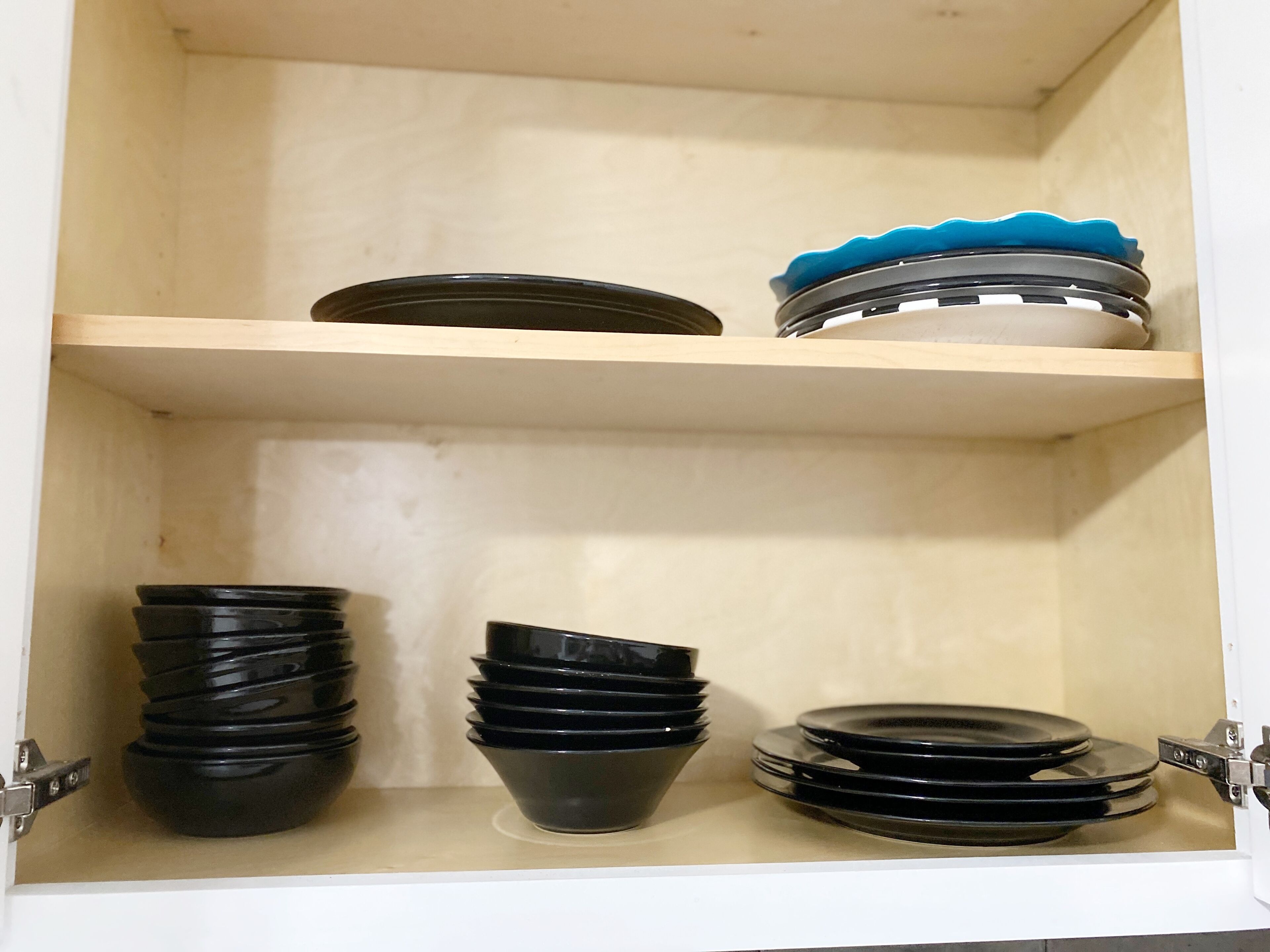 A wooden cabinet with two shelves, each holding black bowls and plates.