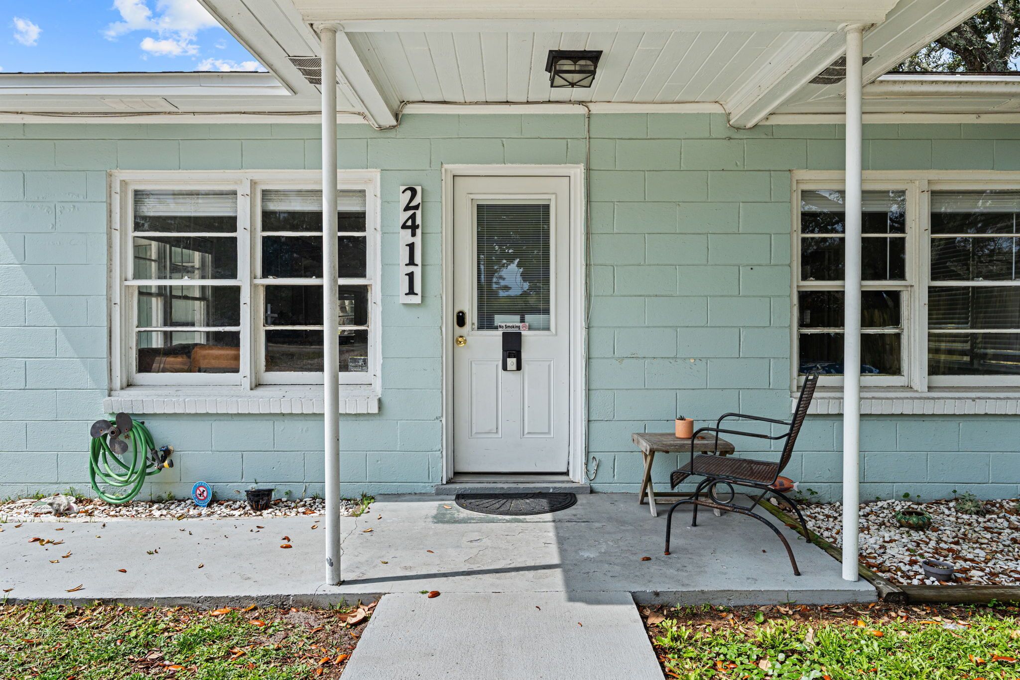 A house with a white door, a number '2411' on the wall, a porch with a bench, and a hose on the ground.