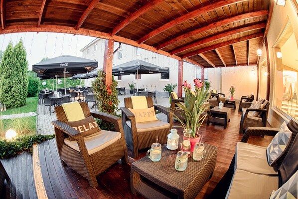 Un patio al aire libre con mobiliario de mimbre, sombrillas y plantas en macetas.
