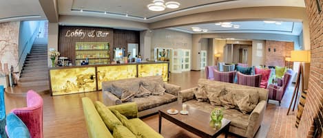 A lobby with a reception desk, sofas, and a staircase.