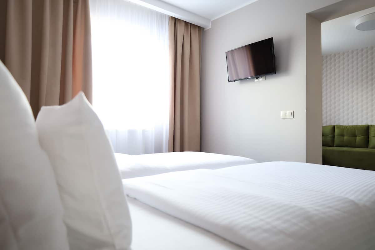 A hotel room with two beds, a flat-screen TV mounted on the wall, and a green upholstered headboard.