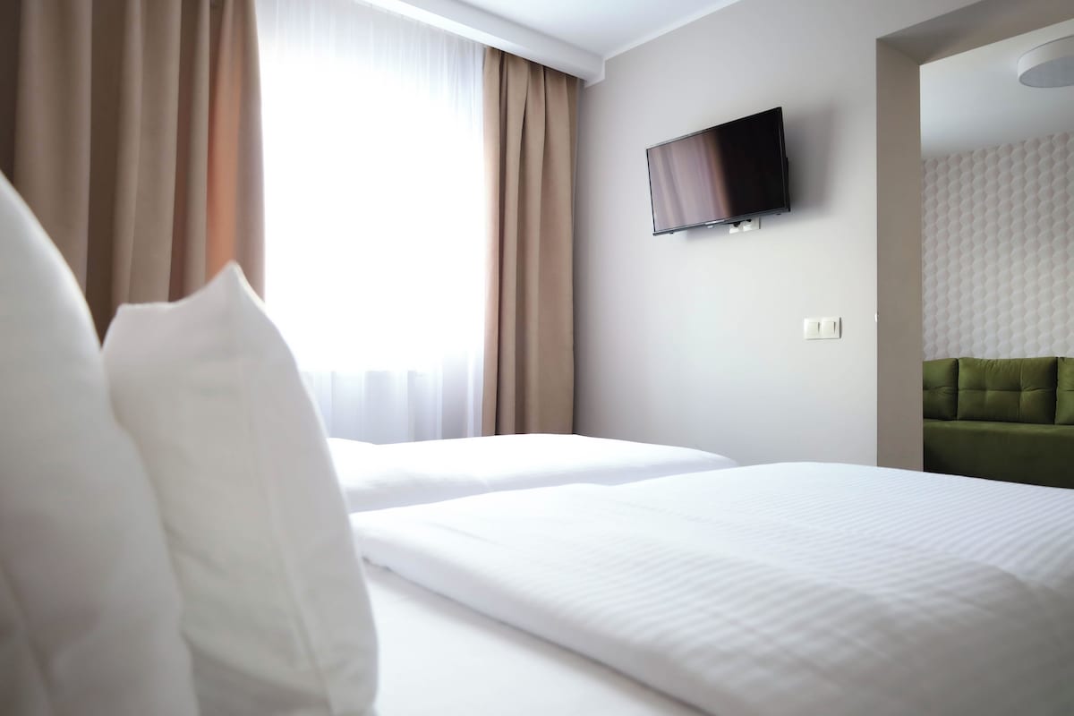 A hotel room with two beds, a flat-screen TV mounted on the wall, and a green upholstered headboard.