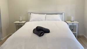Un lit bien fait, avec une literie blanche, deux tables de chevet avec des lampes et un ventilateur de plafond.
