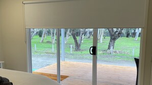 Une chambre avec un lit, un ventilateur de plafond et une vue sur une terrasse extérieure, accessible par une porte-fenêtre coulissante.