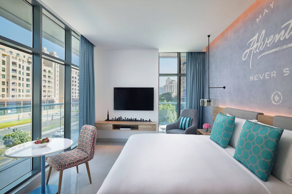 A modern hotel room with a large bed, a TV, a small table, and a chair.
