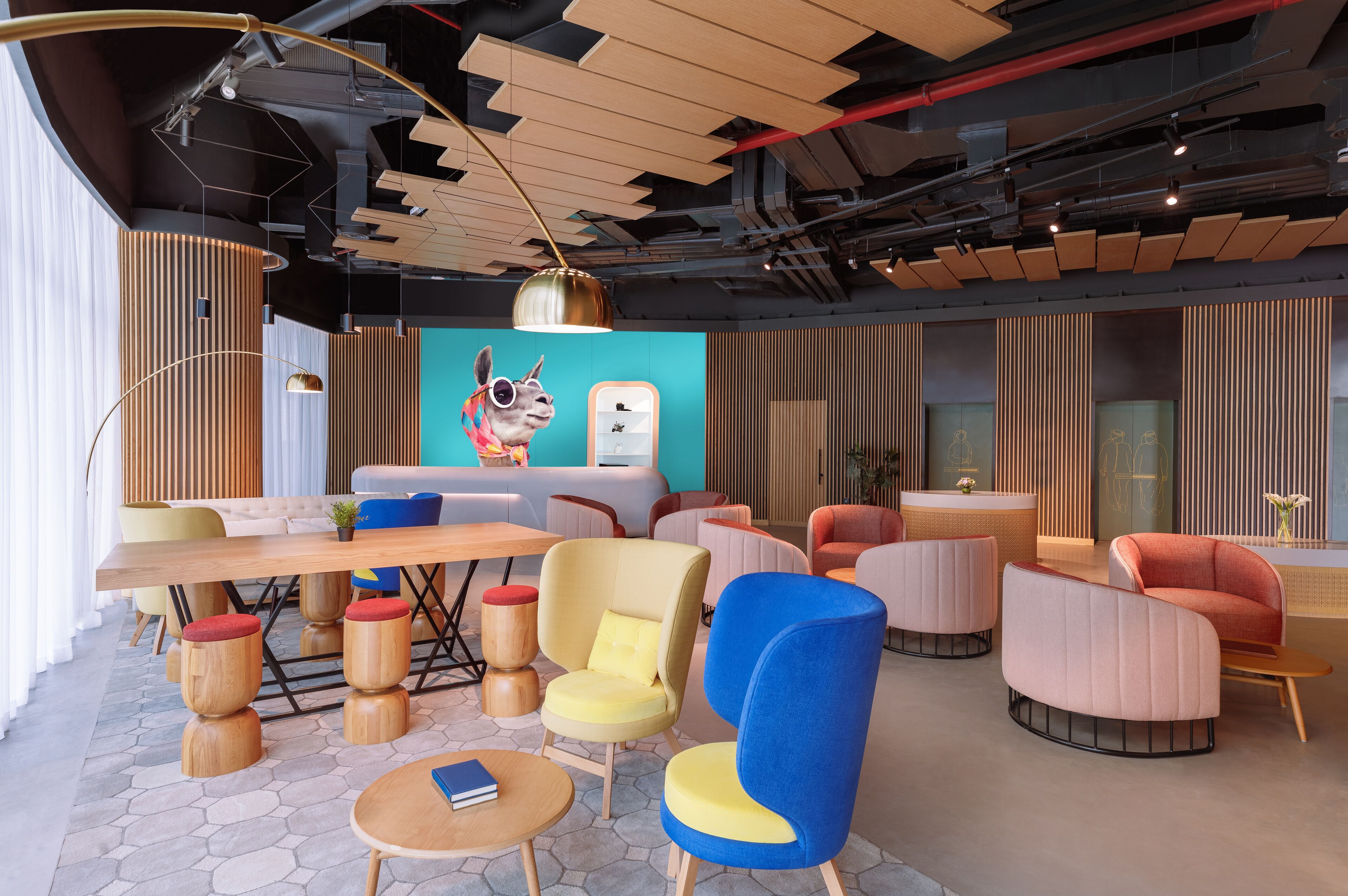 A modern lounge area with a wooden ceiling, a large table, and colorful chairs.