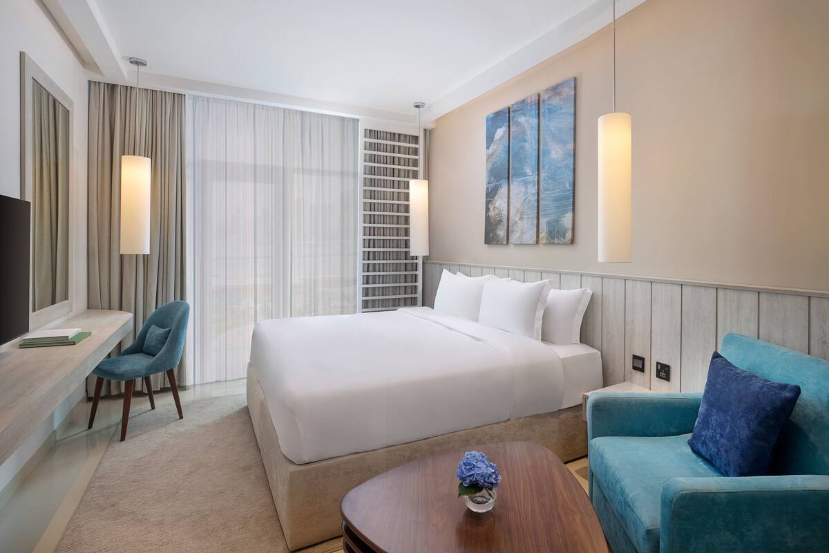 A hotel room with a large bed, a desk with a chair, a sofa, and a coffee table.