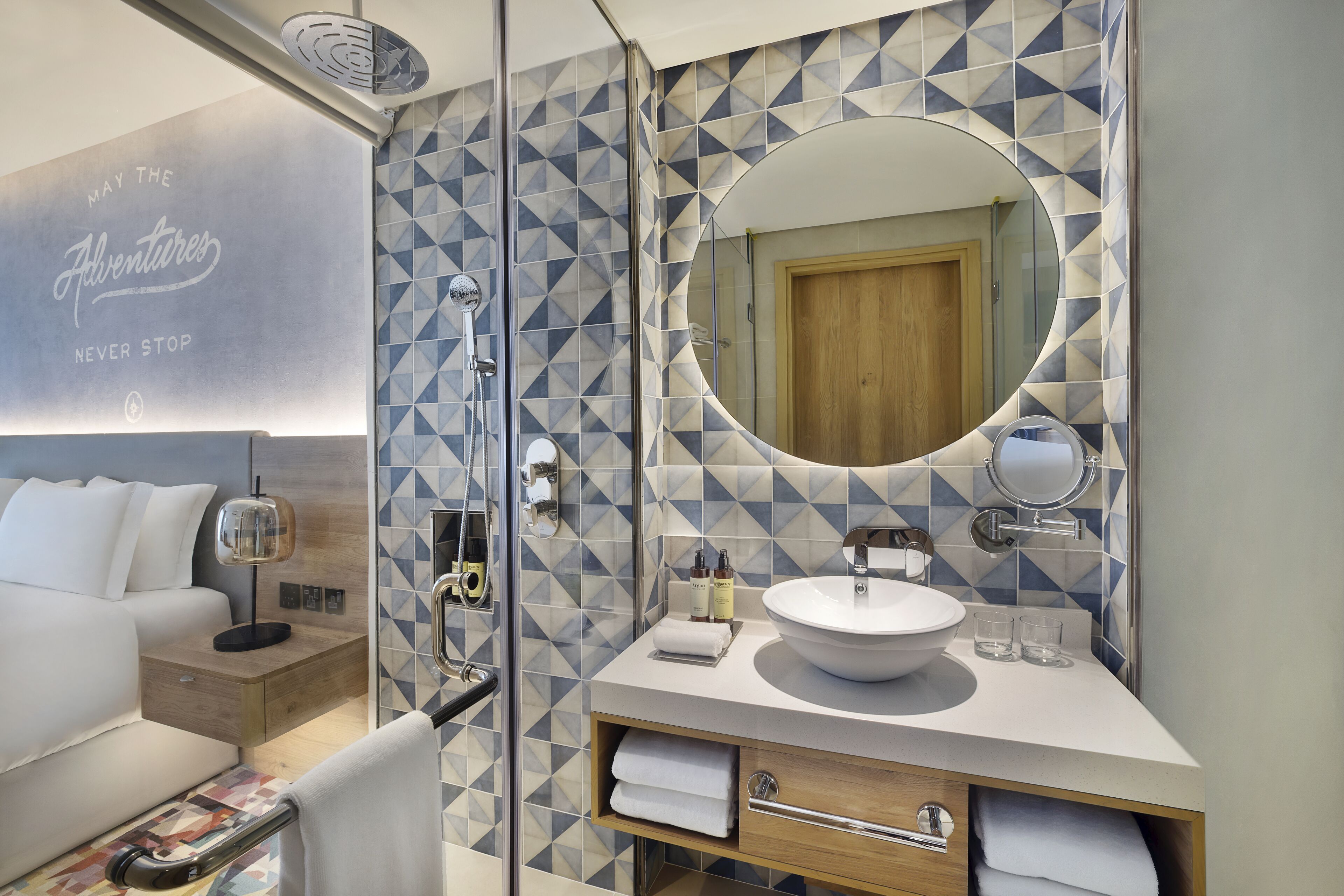 A modern bathroom with a geometric tile backsplash, a round mirror, a sink, and a shower area.