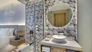Une salle de bain moderne avec un mur recouvert de carreaux aux motifs géométriques, un miroir rond, un lavabo et un espace douche.