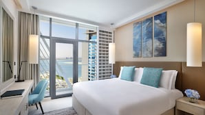 A modern hotel room with a large bed, a desk, and a view of the city through floor-to-ceiling windows. - NH Collection Dubai The Palm (Dubai)