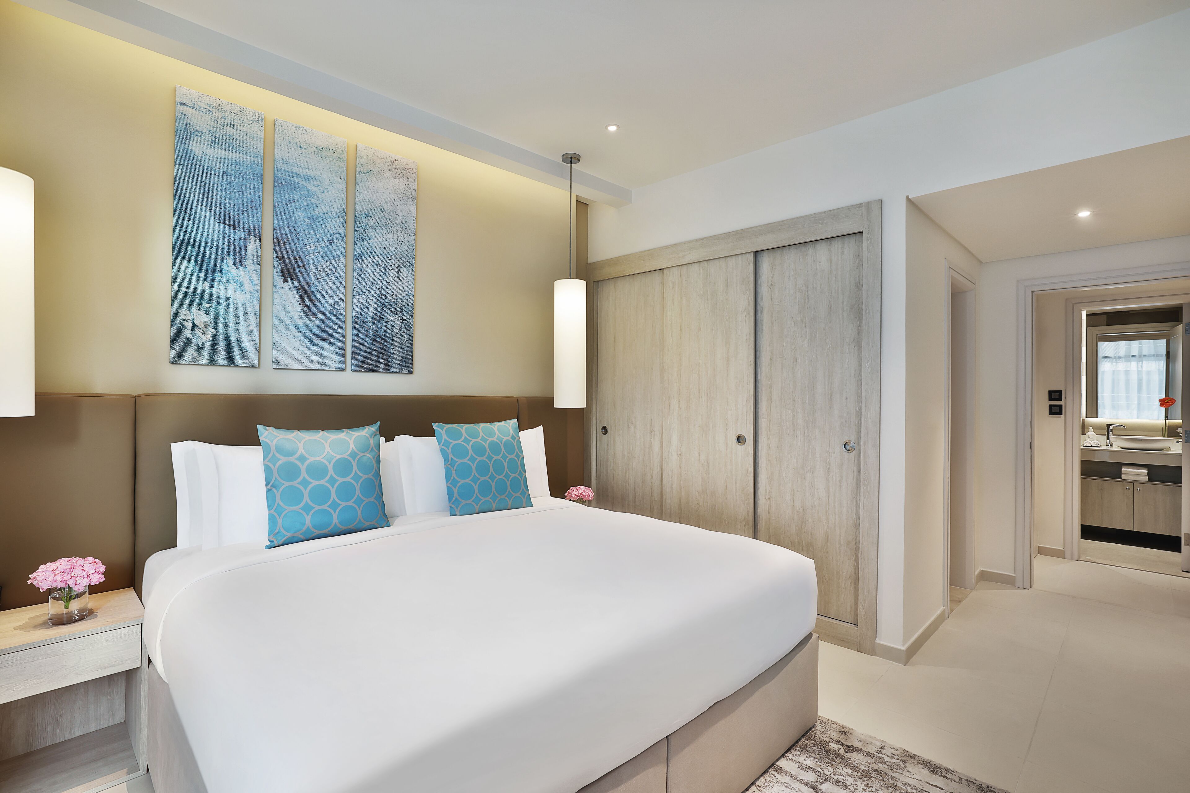 A modern hotel room with a large bed, a wardrobe, and a bathroom visible through an open door.