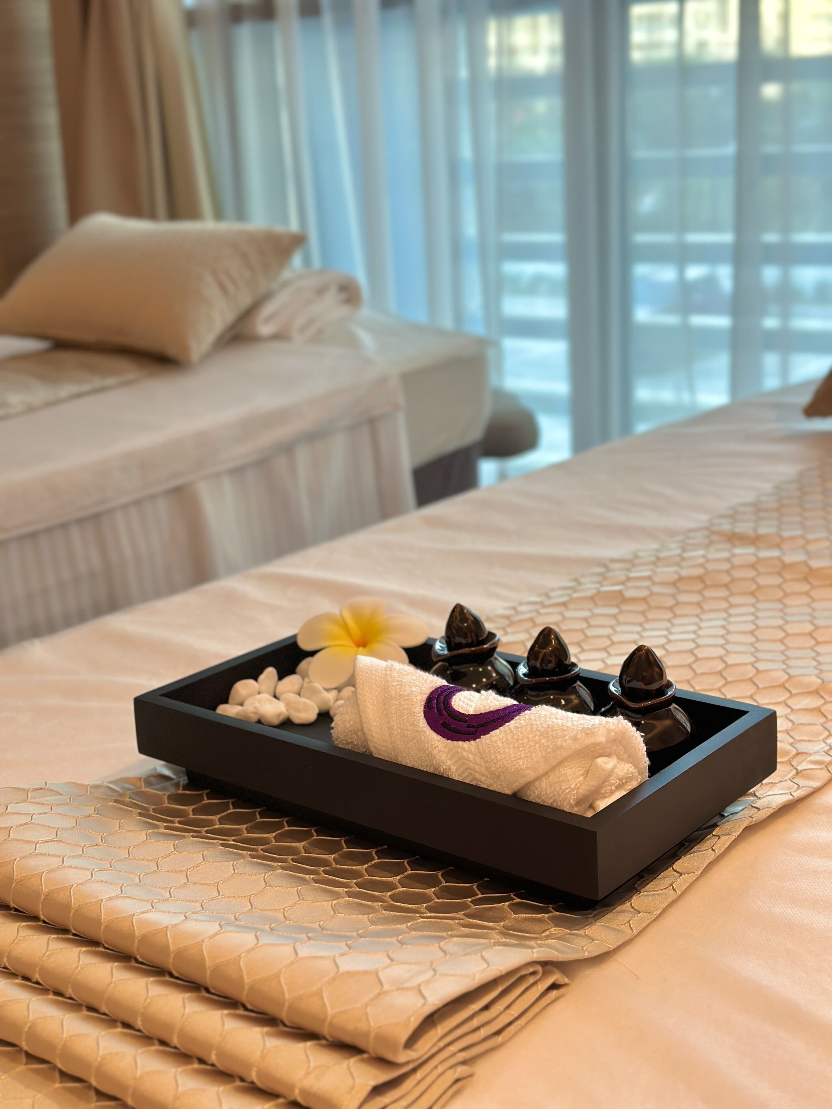 A neatly made bed with a tray of spa items including a towel, flowers, and candles.