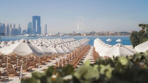 A beach with rows of sun loungers and umbrellas, a Ferris wheel, and a city skyline in the background. - NH Collection Dubai The Palm (Dubai)