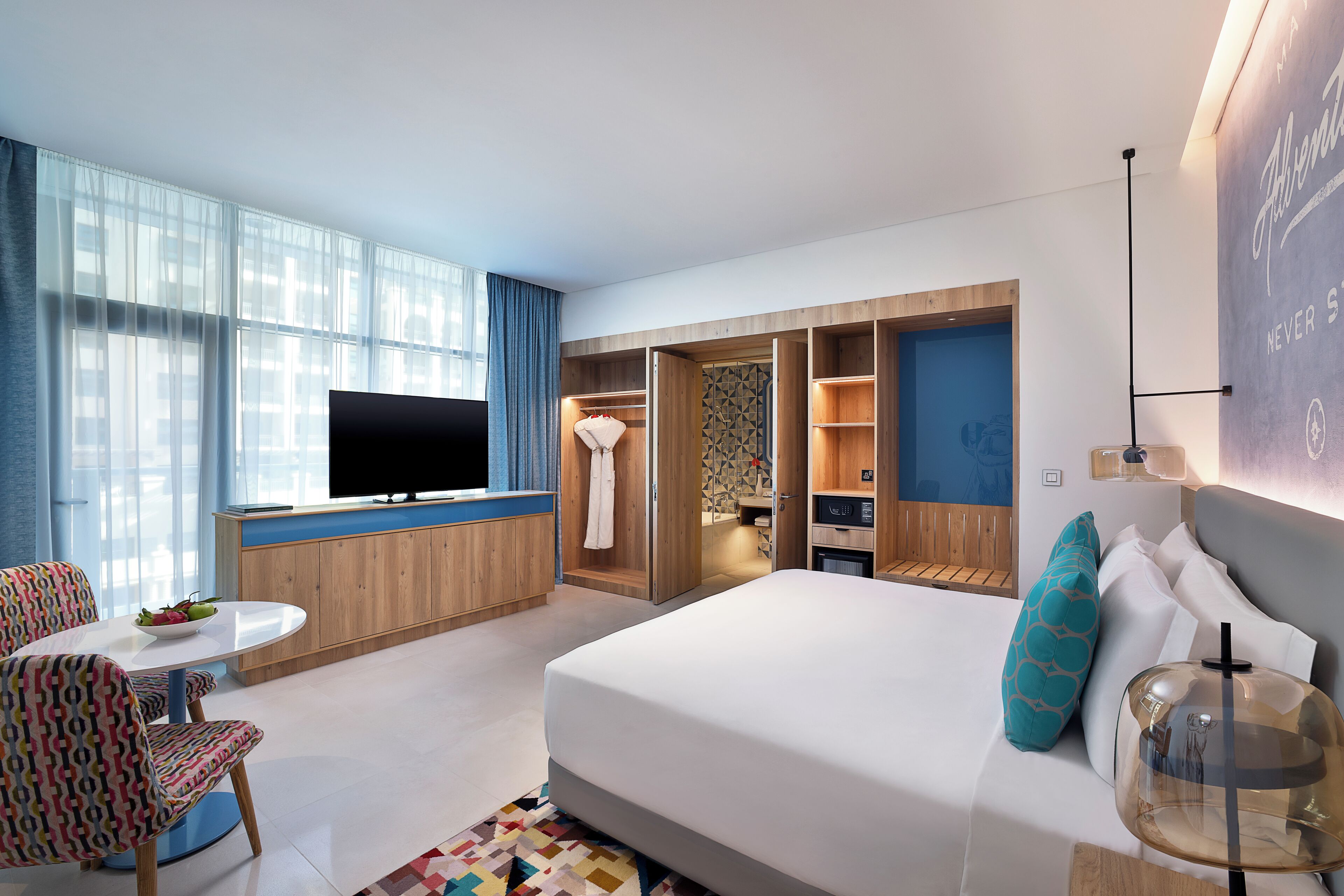 A modern hotel room with a bed, a TV, a dining area, and a walk-in closet.