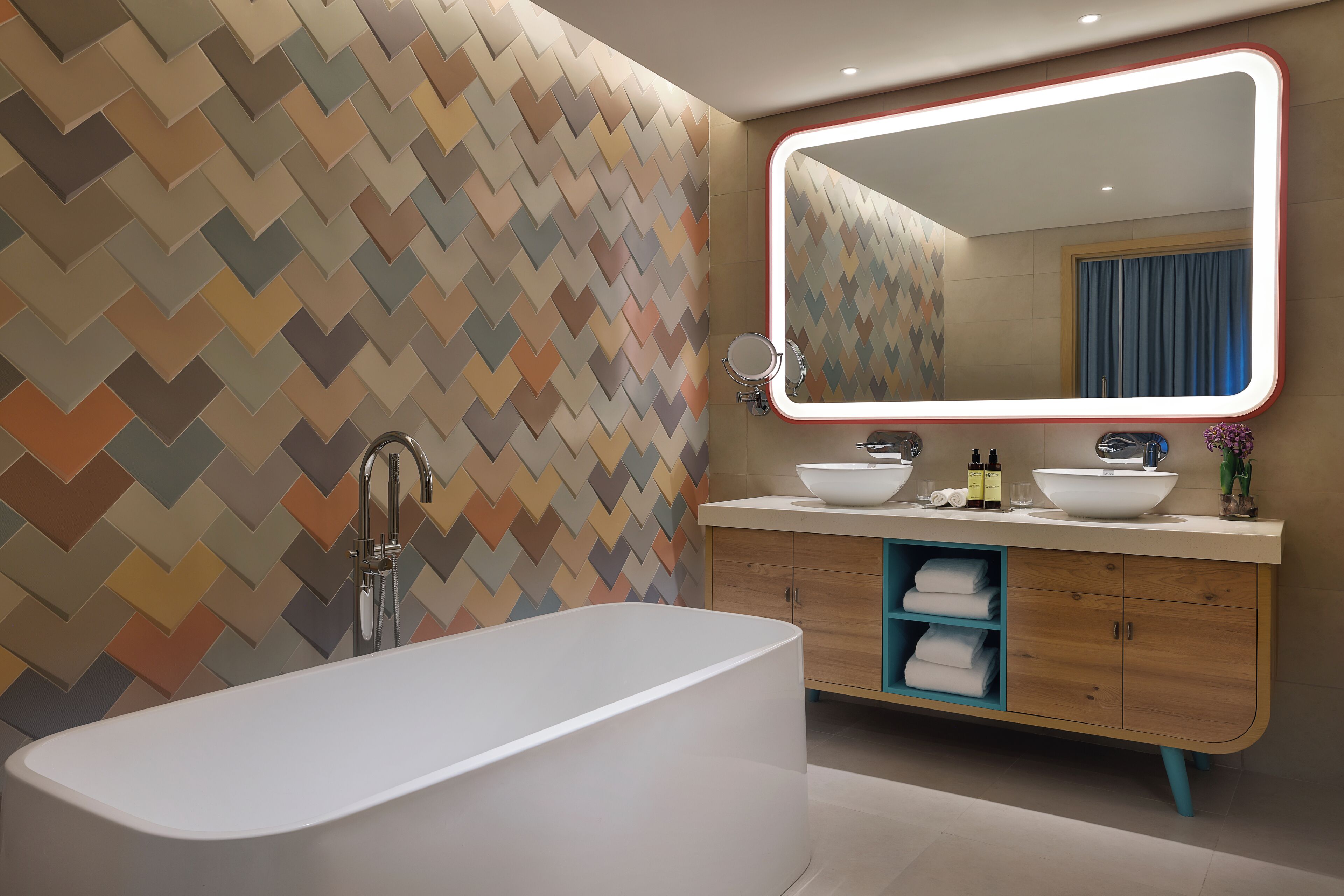 Ein modernes Badezimmer mit einer freistehenden Badewanne, einem Waschtisch mit großem Spiegel und einer Wand mit Zickzackmuster.