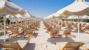 A beach with rows of sun loungers and large umbrellas. - NH Collection Dubai The Palm (Dubai)
