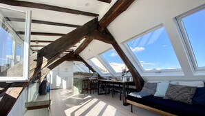 A high-ceilinged room with exposed wooden beams, a skylight, a dining area with a table and chairs, and a sofa with cushions. - Duplex With Terrasse and vue on the Eiffel Tower (Paris)