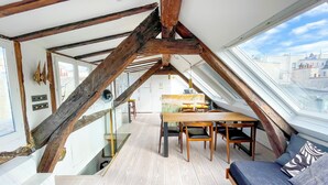 A loft-style room with exposed wooden beams, a wooden dining table, and a sofa. - Duplex With Terrasse and vue on the Eiffel Tower (Paris)