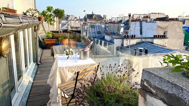 A rooftop terrace with a table set for dining, surrounded by potted plants and overlooking a cityscape. - Duplex With Terrasse and vue on the Eiffel Tower (Paris)