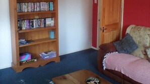 Ein Wohnzimmer mit einer Holzbücherreol, einem Couchtisch aus Holz, einem roten Sofa und einer Tür.