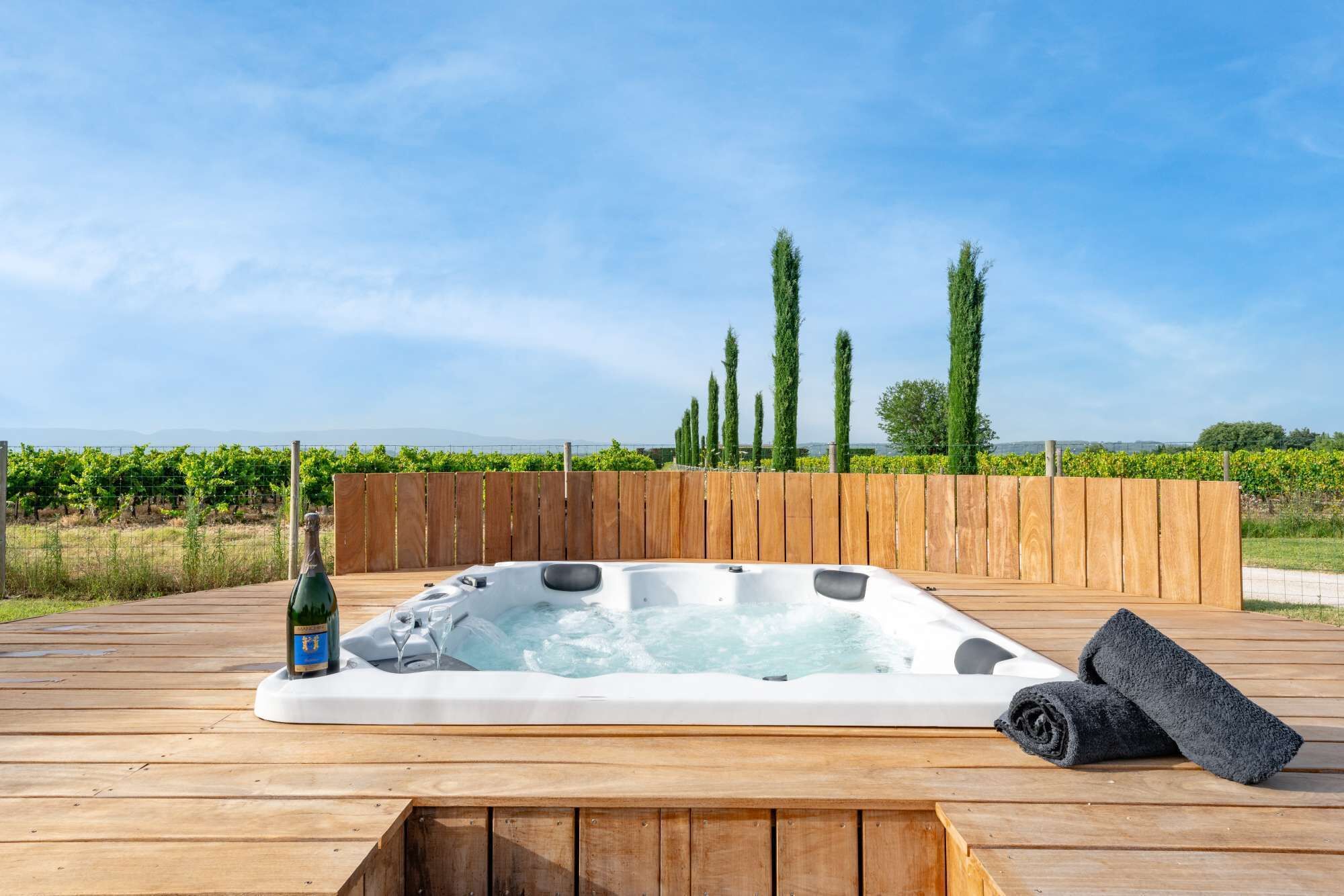 Un bain à remous sur une terrasse en bois, avec une bouteille de champagne et une serviette.
