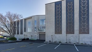 Een modern gebouw met een betonnen gevel, grote ramen en decoratieve metalen panelen.