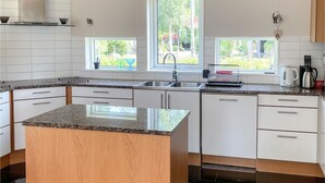 Une cuisine moderne avec des meubles blancs, des plans de travail en granit, un îlot central et une fenêtre donnant sur un espace verdoyant.