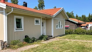 Une maison de plain-pied avec un toit recouvert de tuiles rouges, un porche à l’avant et un chemin en briques menant à l’entrée.
