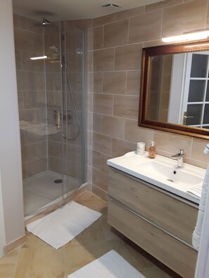 Ein modernes Badezimmer mit Duschkabine aus Glas, einem weißen Waschbecken mit Spiegel und beige gefliesten Wänden.