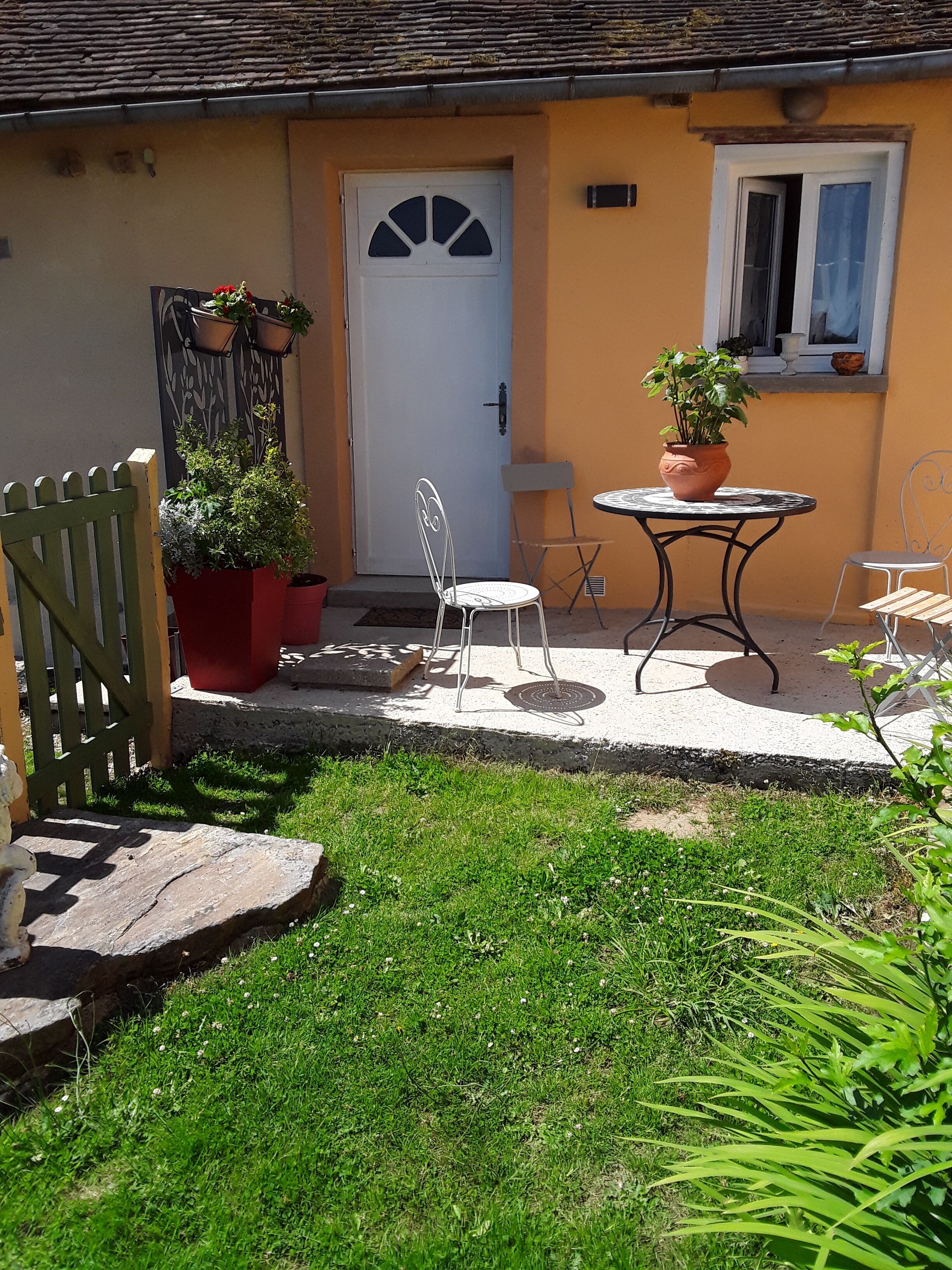 Un pequeño patio con una puerta blanca, una mesita, dos sillas y plantas en macetas.
