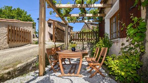 Een buitenzitplaats met een houten pergola, een tafel en stoelen, omringd door geplaveid pad en groen.