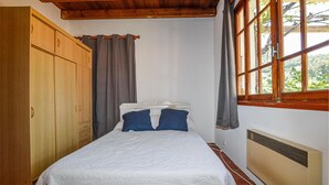 Een slaapkamer met een bed, een houten garderobe, een raam met gordijnen en een radiator.
