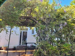 A white building with a covered entrance, surrounded by lush greenery and flowering plants. - Charmante Villa Avec Jardin Arboré Anglet Biarritz (Anglet)
