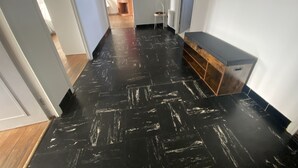 Um corredor com piso em padrão preto e branco, um banco de madeira e uma parede vermelha ao fundo.