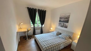 Um quarto pequeno e bem organizado, com cama, escrivaninha, cadeira e duas luminárias de cabeceira.