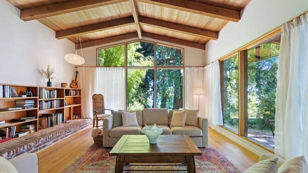 Un salon spacieux avec un haut plafond en bois, de grandes fenêtres, un canapé, une table basse et une bibliothèque remplie de livres.