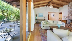 Un vaste espace de vie doté d’un plafond en bois, d’une cheminée en briques et d’une vue sur un patio extérieur aménagé avec des tables et des chaises.
