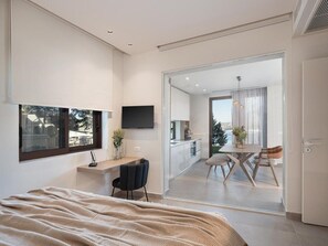 Et moderne soveværelse med en stor seng, et skrivebord med stol, et TV ophængt på væggen og en balkon med spisebord og stole.