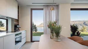 A modern kitchen with a dining area, large windows, and a view of a lake and mountains.