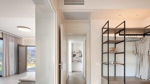 A modern hotel room with a large sliding door leading to a balcony, a walk-in closet with shelves, and a view of the outdoors.