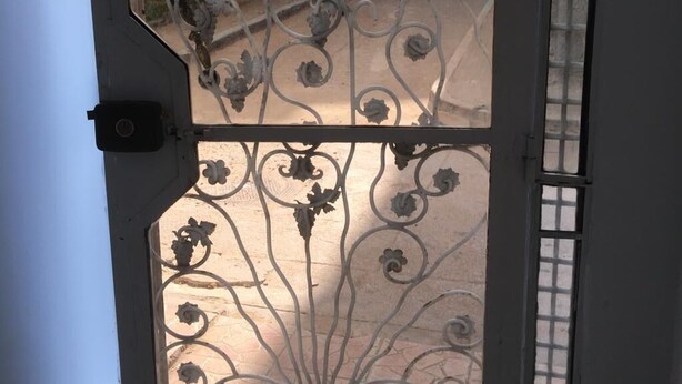 A wrought iron gate with floral designs, a window with a grid pattern, and a view of a building with balconies. - Belgium district (Tanger)
