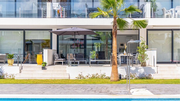 Un edificio moderno con piscina, asientos al aire libre y una palmera.