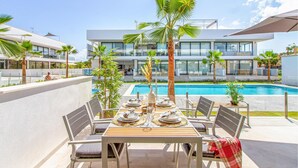 Un área de comedor con una mesa lista para cuatro personas, con vista a una piscina, y edificios modernos al fondo.