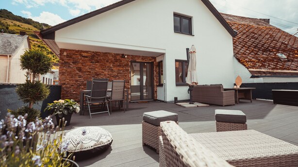 Ein modernes Haus mit einer Terrassenanlage, die Gartenmöbel, eine Steinmauer und einen Blick auf die umliegende Landschaft bietet.