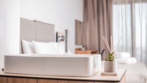 A modern bathroom with a white sink, a shower, and a bedside table with a plant.