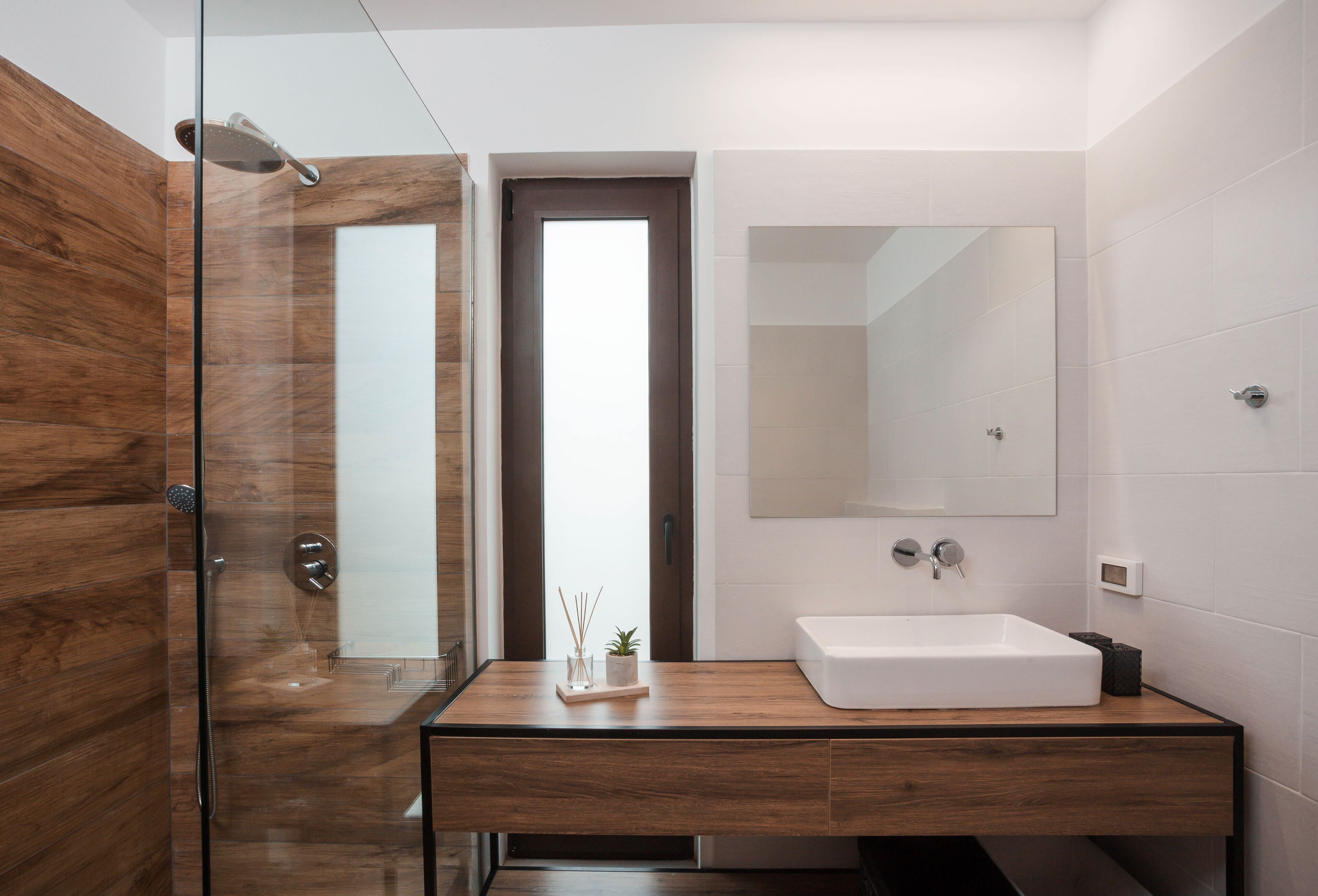 A modern bathroom with a wooden vanity, a large mirror, and a glass shower enclosure.