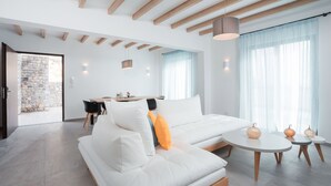 A modern living room with a white sofa, a dining area, and a stone wall.